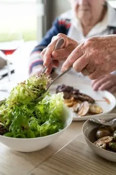 Personne âgée se servant de la salade à table lors d'un repas : aide aux repas